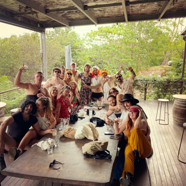 Group of people in casual clothes posing around a long table on a covered patio.