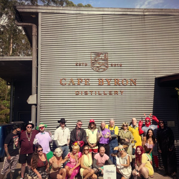 Group of people in colorful costumes posing in front of Cape Byron Distillery building.