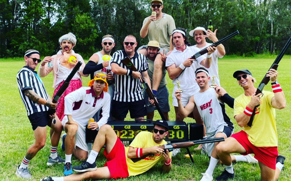 Group of men in costumes holding toy guns and props outdoors on grass.