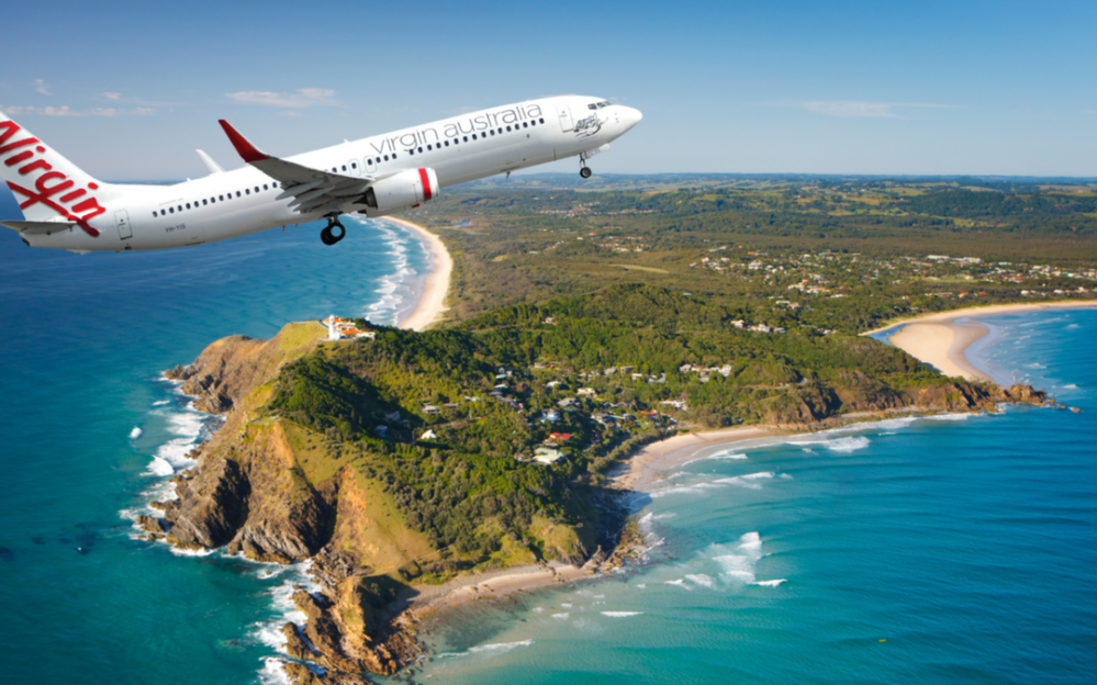 Airplane flying over coastline with green hills and ocean.